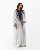Model in the pearl-white Royal Bisht of Alnaqab abaya — open robe with embroidered front bands and wide cape sleeves — ASHI